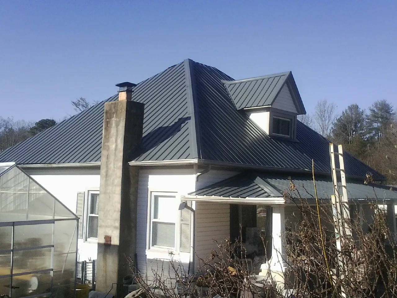 Dark blue standing seam metal roof on a white farmhouse with dormer — Slate & Tile Roof Repair by Roofing Brothers in Cassville