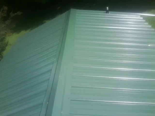 New green metal panels meeting at the ridge of a roof — Flat Roof Repair work by our crew in Cassville