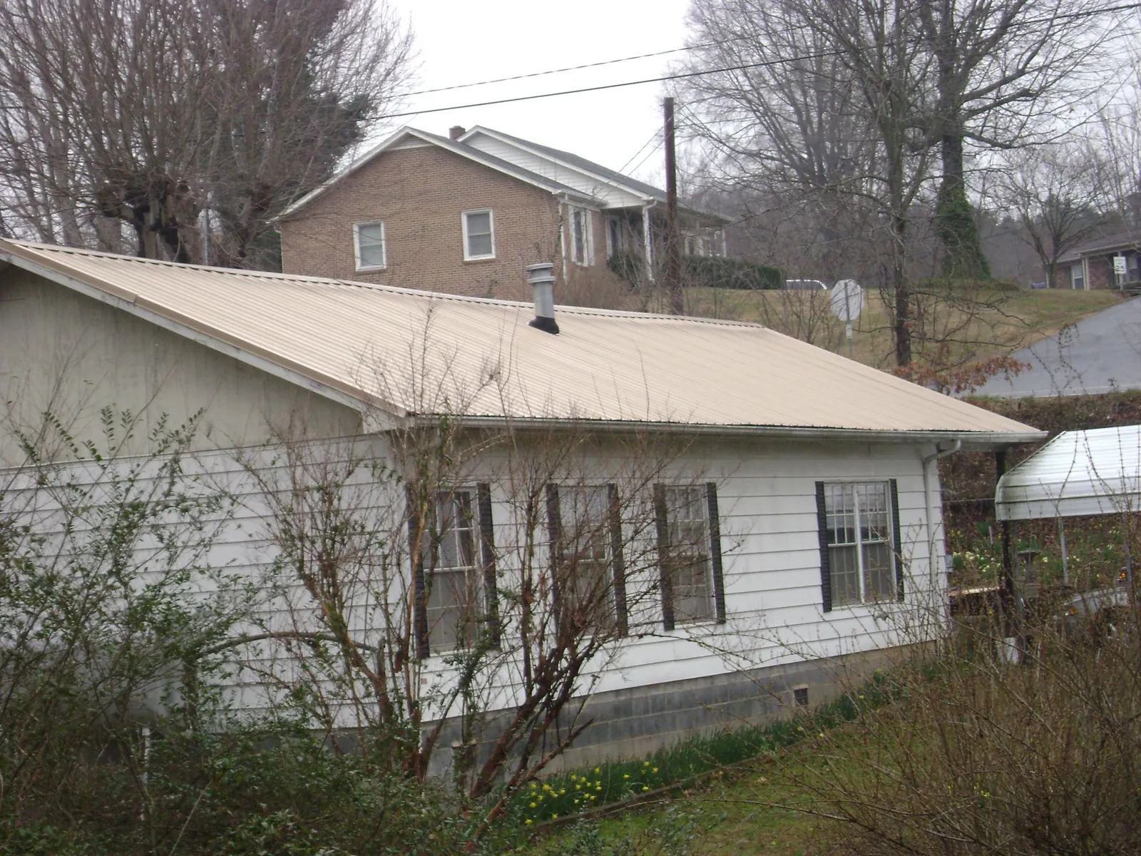 Tan metal roof on a white sided house set into a hillside — Commercial Roofing by Roofing Brothers in Cassville